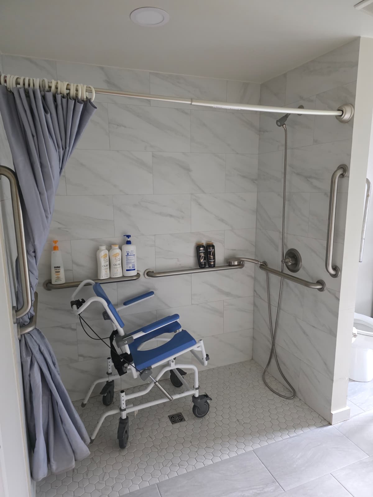 An older man smiles while exercising with pink dumbbells, assisted by a woman in a light blue hoodie, reflecting the supportive environment of all-inclusive senior care in Snohomish County inside a bright room with large windows.